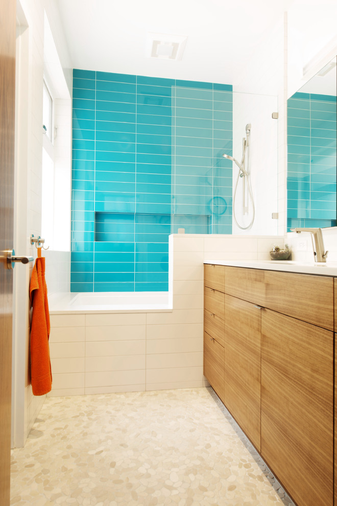 Immagine di una stanza da bagno con doccia moderna con ante lisce, vasca ad alcova, vasca/doccia, piastrelle blu, pavimento con piastrelle di ciottoli e ante in legno chiaro