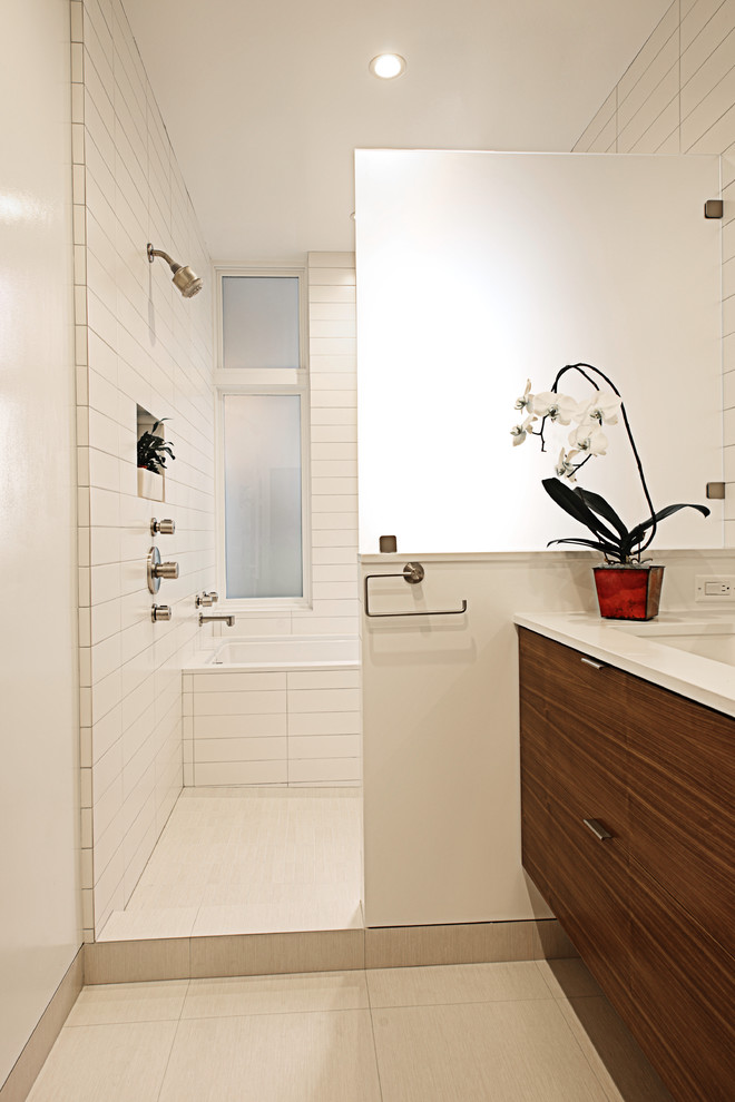 Bild på ett tropiskt badrum, med ett undermonterad handfat, släta luckor, skåp i mörkt trä, ett undermonterat badkar och vit kakel
