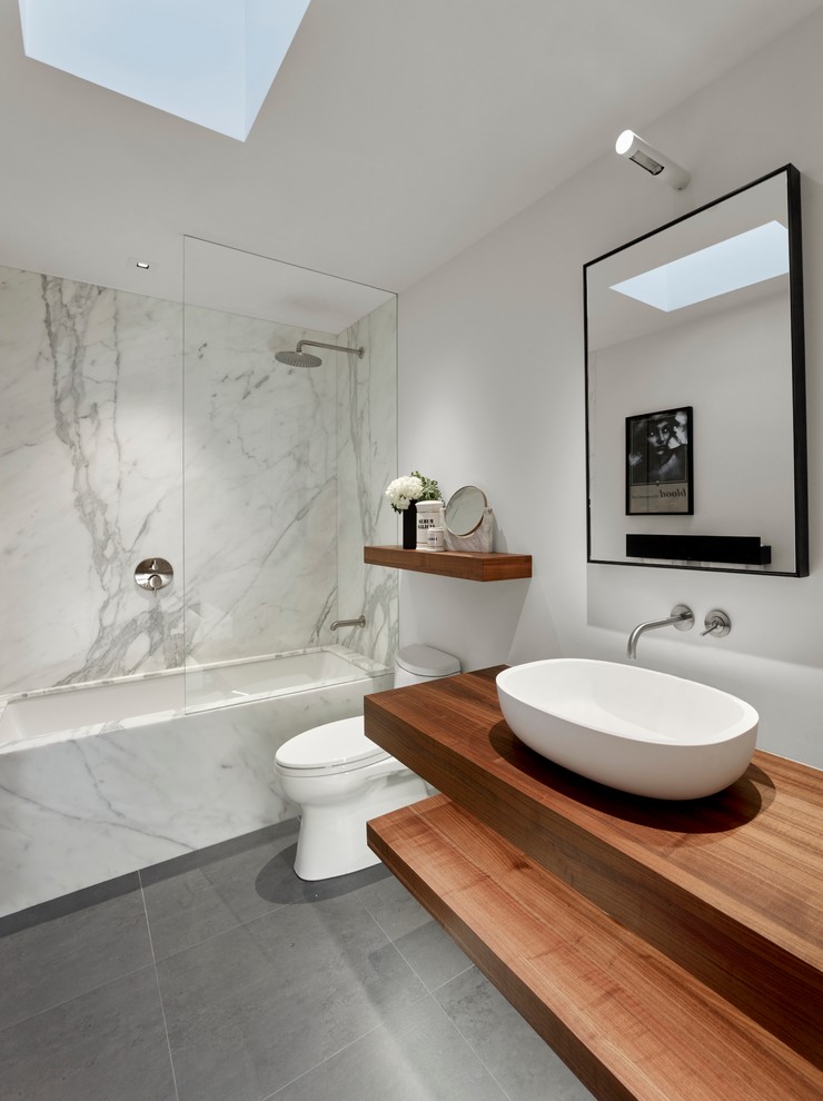 Inredning av ett modernt badrum, med ett undermonterat badkar, en dusch/badkar-kombination, vit kakel, vita väggar, ett fristående handfat, träbänkskiva och med dusch som är öppen