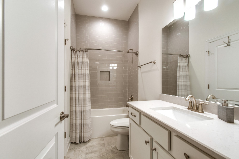ナッシュビルにある高級な中くらいなトランジショナルスタイルのおしゃれなバスルーム (浴槽なし) (グレーのタイル、セラミックタイル、グレーの壁、セラミックタイルの床、アンダーカウンター洗面器、御影石の洗面台、マルチカラーの床、白い洗面カウンター、洗面台2つ、造り付け洗面台、シェーカースタイル扉のキャビネット、白いキャビネット、アルコーブ型浴槽、シャワー付き浴槽	、分離型トイレ、シャワーカーテン、ニッチ、三角天井) の写真