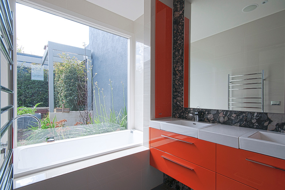 This is an example of a large contemporary ensuite bathroom in Melbourne with flat-panel cabinets, orange cabinets, a built-in bath, beige tiles, ceramic tiles, engineered stone worktops, an alcove shower, beige walls, porcelain flooring, an integrated sink, grey floors and an open shower.