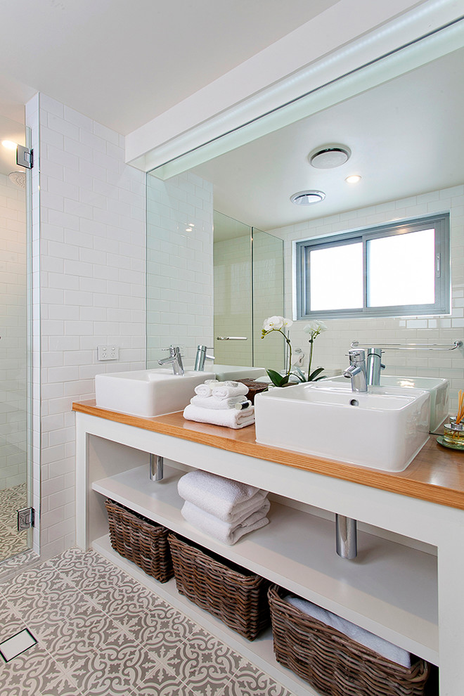 Exemple d'une petite douche en alcôve principale exotique avec un placard sans porte, des portes de placard blanches, WC à poser, un carrelage beige, un mur blanc, un sol en carrelage de céramique, une vasque et un plan de toilette en bois.