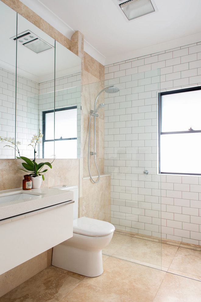 This is an example of a classic bathroom in Brisbane with flat-panel cabinets, white cabinets, a built-in shower, a two-piece toilet, white tiles, metro tiles, beige walls and a submerged sink.