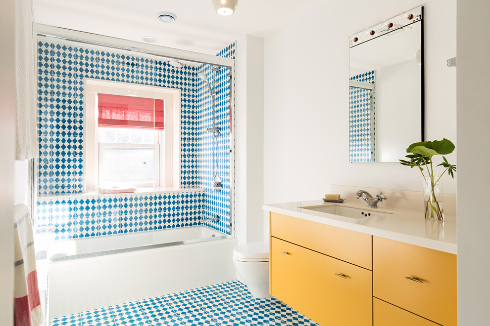 Réalisation d'une salle de bain design avec un placard à porte plane, des portes de placard jaunes, une baignoire en alcôve, un combiné douche/baignoire, WC suspendus, un carrelage bleu, un carrelage multicolore, un carrelage blanc, un mur blanc, un lavabo encastré, une cabine de douche à porte coulissante et du carrelage bicolore.