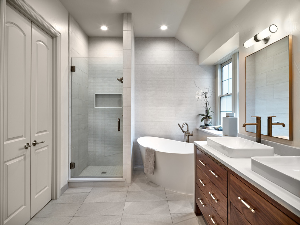 Idéer för ett mellanstort klassiskt vit en-suite badrum, med släta luckor, ett fristående badkar, vit kakel, porslinskakel, vita väggar, klinkergolv i porslin, ett fristående handfat, bänkskiva i kvarts, grått golv, dusch med gångjärnsdörr, skåp i mellenmörkt trä och en dusch i en alkov