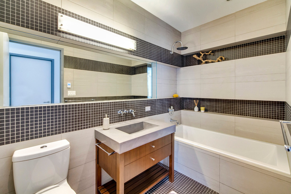 Modern inredning av ett mellanstort en-suite badrum, med skåp i mörkt trä, bänkskiva i betong, ett badkar i en alkov, en toalettstol med separat cisternkåpa, grå kakel, porslinskakel, mosaikgolv, ett integrerad handfat, en dusch/badkar-kombination och släta luckor