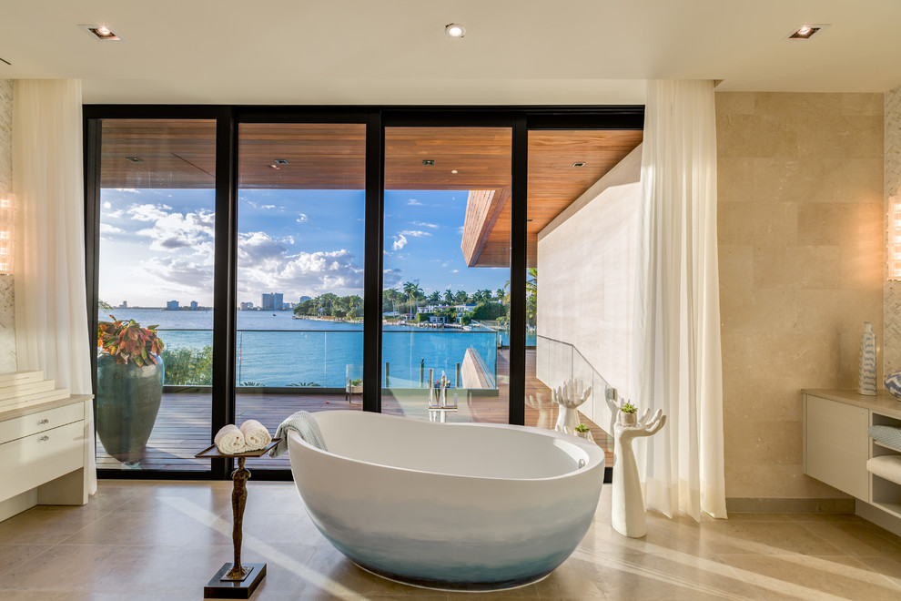 Modernes Badezimmer mit flächenbündigen Schrankfronten, beigen Schränken, freistehender Badewanne, braunen Fliesen und beigem Boden in Miami