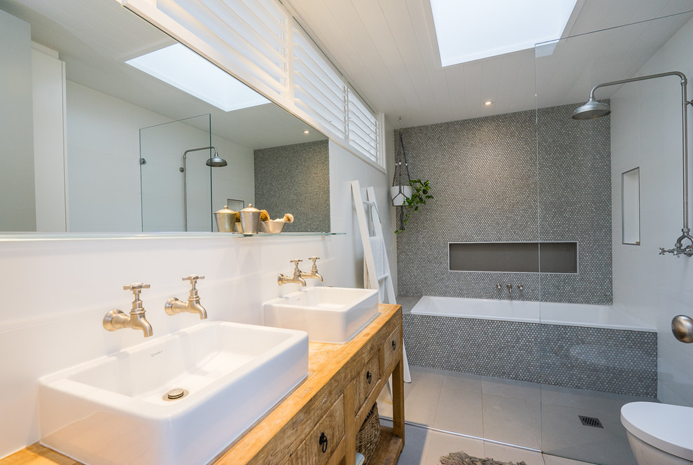 Cette photo montre une salle de bain principale bord de mer en bois brun avec une baignoire en alcôve, une douche ouverte, un mur gris, une vasque, un sol blanc, aucune cabine et un placard à porte plane.