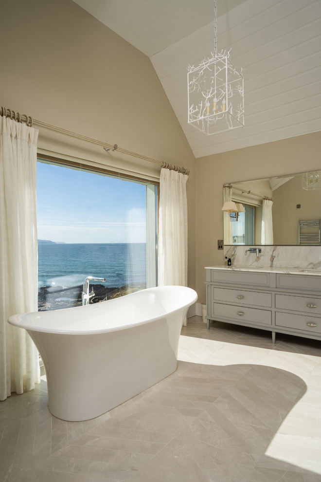 На фото: большая ванная комната в стиле кантри с фасадами с утопленной филенкой, серыми фасадами, отдельно стоящей ванной, коричневыми стенами, мраморной столешницей и белой столешницей