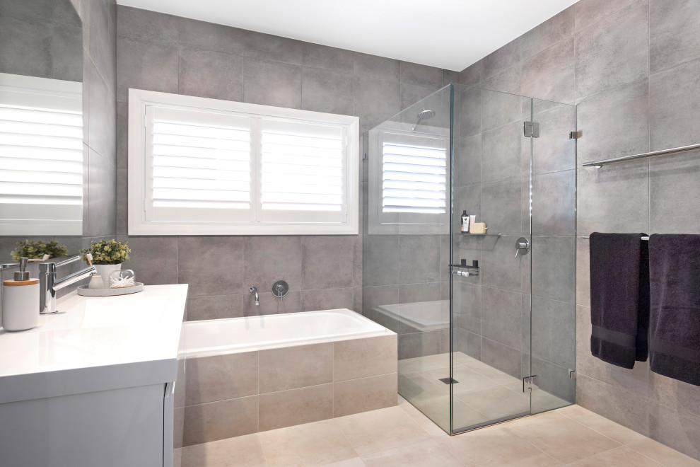 Inredning av ett modernt vit vitt badrum, med släta luckor, vita skåp, ett platsbyggt badkar, en kantlös dusch, grå kakel, ett integrerad handfat, beiget golv och dusch med gångjärnsdörr