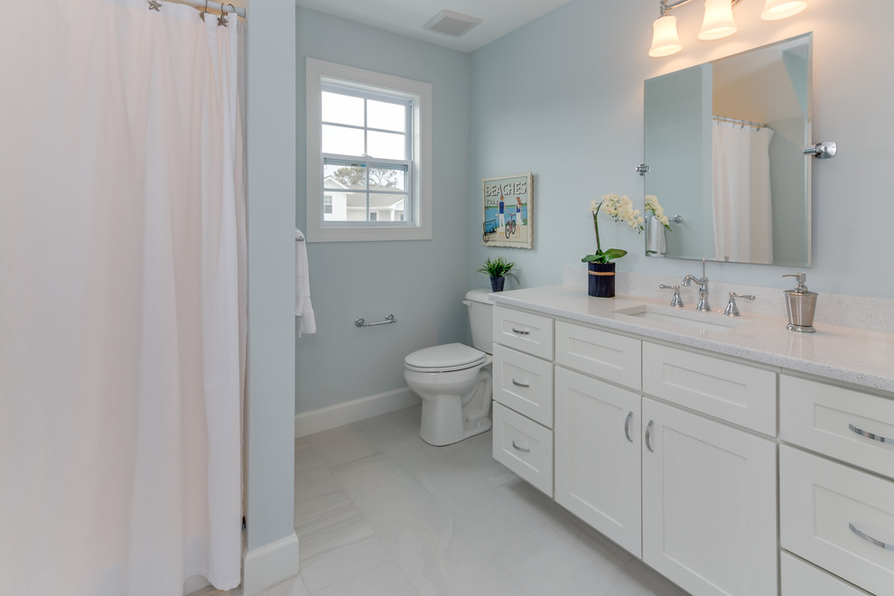 Foto på ett mellanstort maritimt gul badrum för barn, med skåp i shakerstil, vita skåp, en dusch/badkar-kombination, en toalettstol med hel cisternkåpa, blå väggar, klinkergolv i keramik, ett undermonterad handfat, marmorbänkskiva, grått golv och dusch med duschdraperi