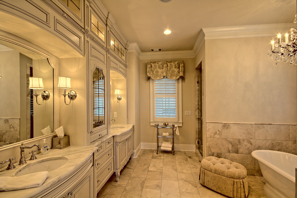 Large traditional ensuite bathroom in Atlanta with recessed-panel cabinets, distressed cabinets, a freestanding bath, porcelain tiles, beige walls, porcelain flooring, a submerged sink and marble worktops.