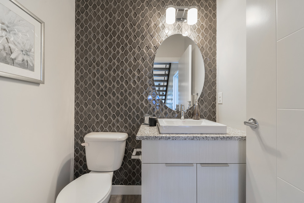 Idéer för att renovera ett litet funkis grå grått badrum, med släta luckor, vita skåp, en toalettstol med separat cisternkåpa, vit kakel, keramikplattor, vita väggar, laminatgolv, ett nedsänkt handfat, granitbänkskiva och grått golv