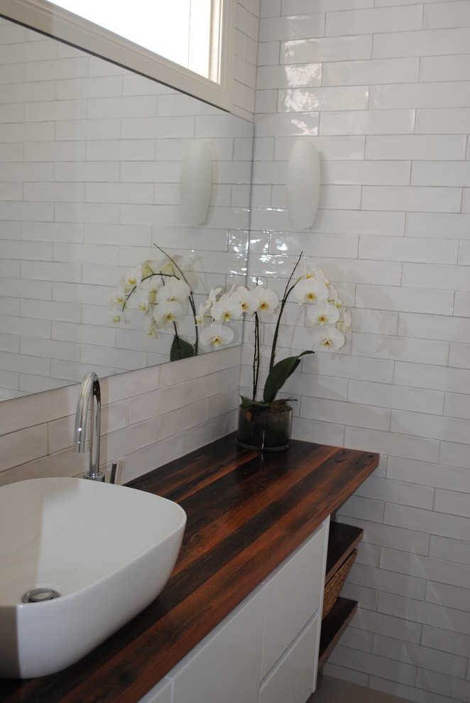 Idéer för ett mellanstort modernt en-suite badrum, med möbel-liknande, vita skåp, en öppen dusch, en toalettstol med hel cisternkåpa, vit kakel, keramikplattor, vita väggar, klinkergolv i porslin, ett fristående handfat och träbänkskiva
