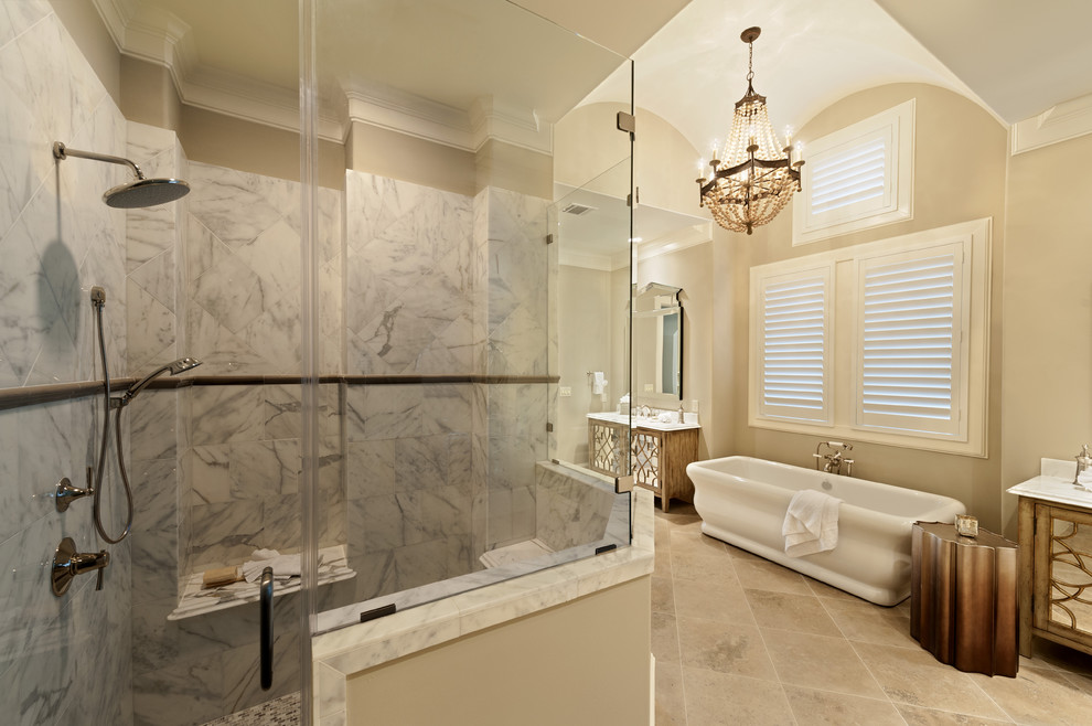 This is an example of a large traditional ensuite bathroom in Houston with freestanding cabinets, medium wood cabinets, a freestanding bath, a corner shower, grey tiles, marble tiles, beige walls, marble flooring, a submerged sink, marble worktops, beige floors and a hinged door.