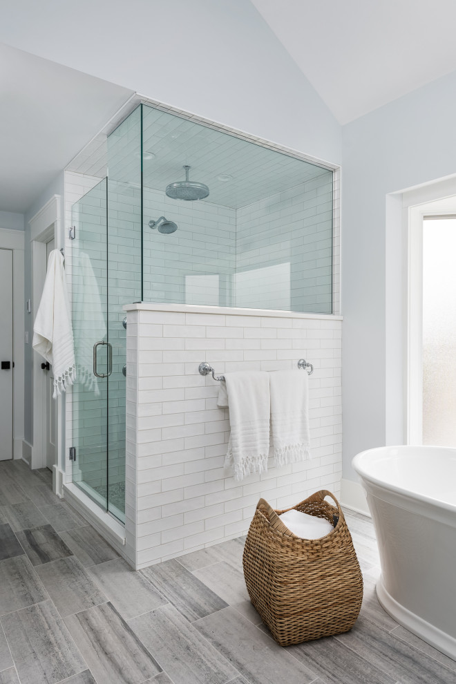 На фото: большая главная ванная комната в стиле кантри с плоскими фасадами, синими фасадами, отдельно стоящей ванной, угловым душем, раздельным унитазом, белой плиткой, керамогранитной плиткой, белыми стенами, полом из керамогранита, врезной раковиной, столешницей из искусственного кварца, серым полом, душем с распашными дверями, белой столешницей, сиденьем для душа, тумбой под две раковины и встроенной тумбой с