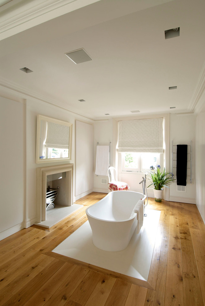 Ejemplo de cuarto de baño actual con bañera exenta, paredes blancas y suelo de madera en tonos medios