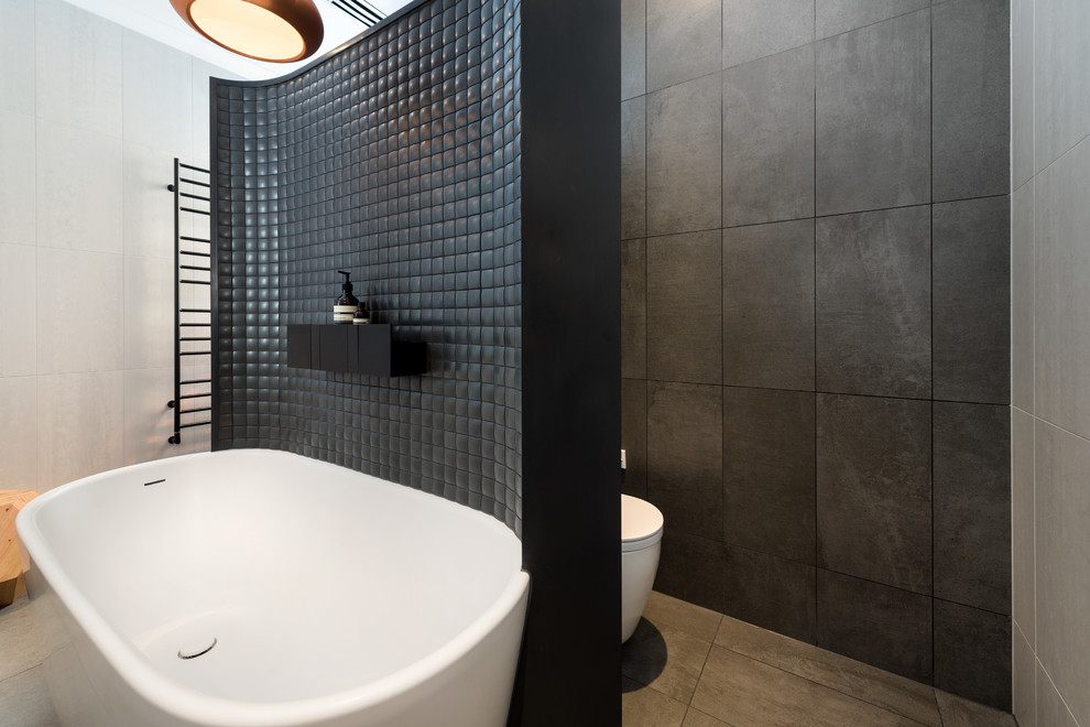 Foto på ett funkis badrum, med ett fristående badkar, svart kakel, grå kakel, grå väggar och grått golv