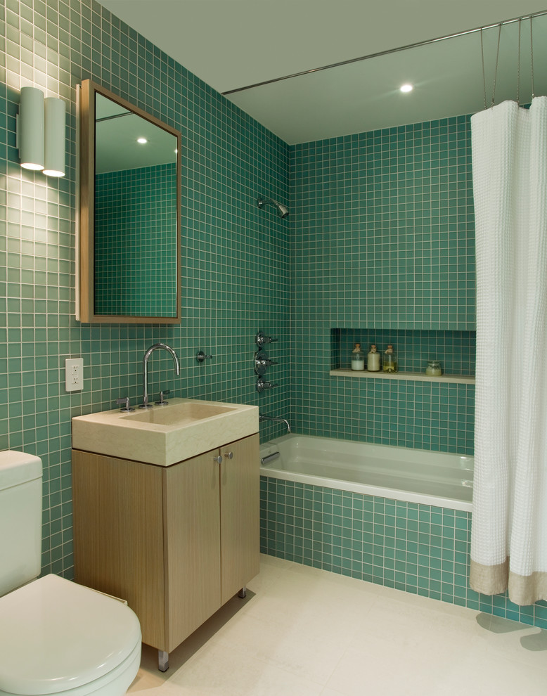 На фото: ванная комната в стиле модернизм с светлыми деревянными фасадами, душем над ванной, синей плиткой, стеклянной плиткой, плоскими фасадами и монолитной раковиной с