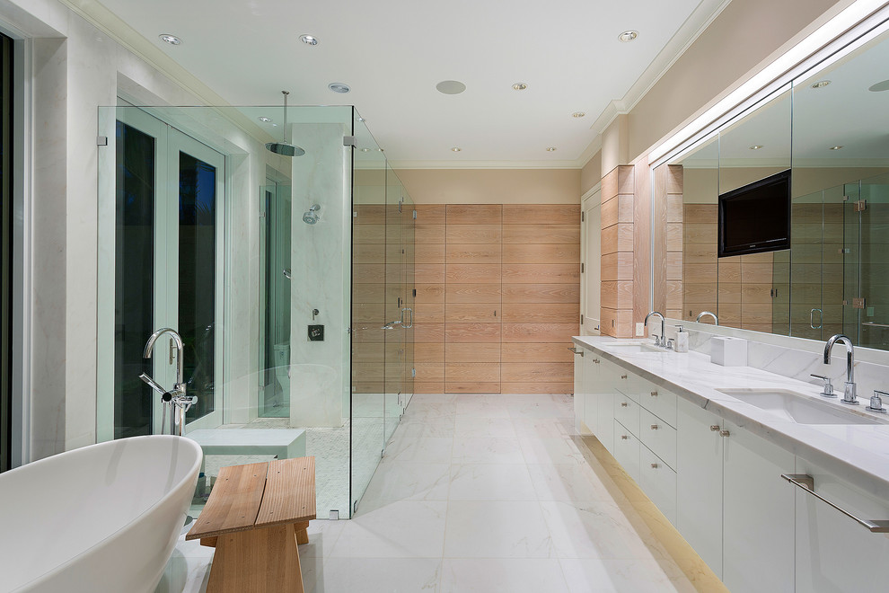 Bild på ett tropiskt en-suite badrum, med släta luckor, vita skåp, ett fristående badkar, en kantlös dusch, vit kakel, beige väggar, ett undermonterad handfat, vitt golv och dusch med gångjärnsdörr