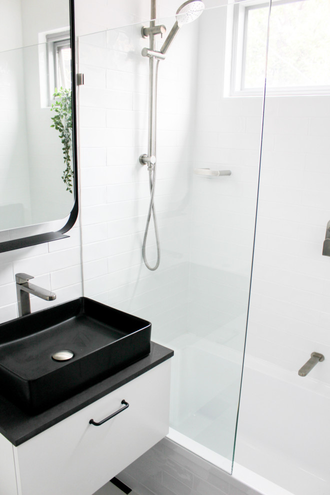 Design ideas for a small modern shower room bathroom in Perth with flat-panel cabinets, white cabinets, an alcove bath, a shower/bath combination, a one-piece toilet, white tiles, ceramic tiles, white walls, porcelain flooring, a vessel sink, engineered stone worktops, multi-coloured floors, black worktops, a single sink and a floating vanity unit.