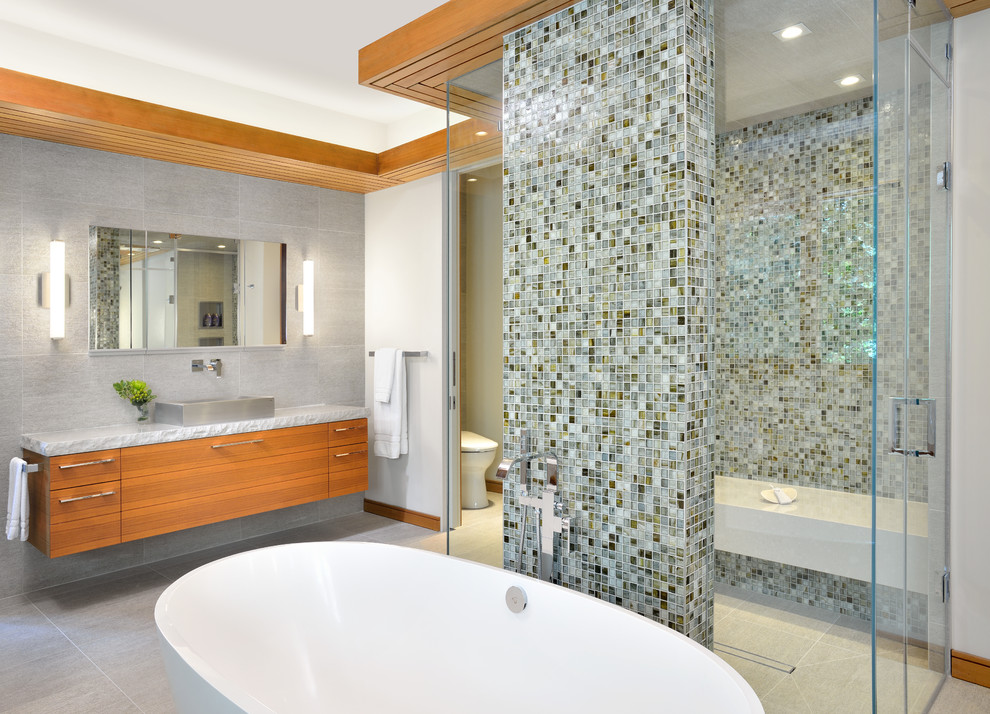 This is an example of an expansive contemporary ensuite bathroom in Toronto with a vessel sink, flat-panel cabinets, medium wood cabinets, a freestanding bath, a built-in shower, multi-coloured tiles, mosaic tiles, beige walls, a two-piece toilet and porcelain flooring.