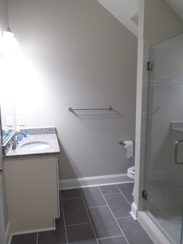 Exempel på ett mellanstort klassiskt badrum för barn, med ett undermonterad handfat, luckor med infälld panel, vita skåp, granitbänkskiva, en dusch i en alkov, en toalettstol med hel cisternkåpa, grå kakel, porslinskakel, grå väggar och klinkergolv i porslin