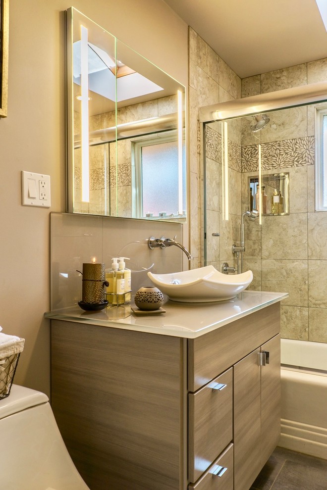Inredning av ett modernt litet badrum, med släta luckor, beige skåp, en dusch/badkar-kombination, en toalettstol med separat cisternkåpa, beige kakel, beige väggar, klinkergolv i keramik, ett fristående handfat, bänkskiva i glas, grått golv och dusch med skjutdörr