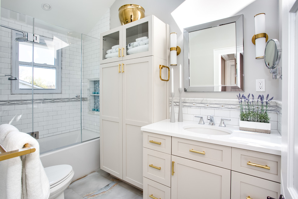 На фото: главная ванная комната в стиле неоклассика (современная классика) с фасадами в стиле шейкер, серыми фасадами, ванной в нише, душем над ванной, раздельным унитазом, белой плиткой, плиткой кабанчик, серыми стенами, полом из керамогранита, врезной раковиной, столешницей из искусственного кварца, разноцветным полом, душем с распашными дверями и белой столешницей с