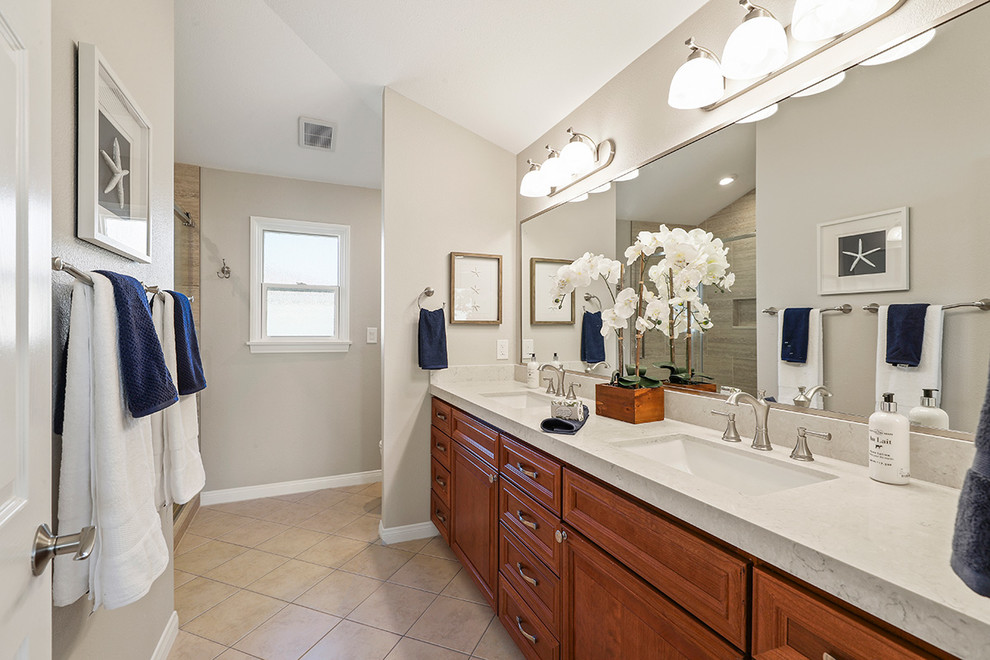 Inspiration for a medium sized traditional ensuite bathroom in Orange County with recessed-panel cabinets, medium wood cabinets, an alcove shower, a one-piece toilet, beige tiles, porcelain tiles, grey walls, travertine flooring, a submerged sink, engineered stone worktops, beige floors, a sliding door and beige worktops.