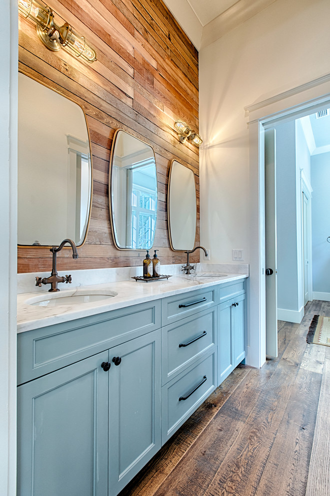 Cette photo montre une salle d'eau nature avec un placard avec porte à panneau encastré, des portes de placard bleues, un mur blanc, un sol en bois brun, un lavabo encastré et un sol marron.
