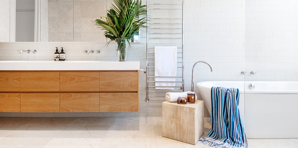 Cette image montre une salle de bain principale design en bois brun de taille moyenne avec une baignoire indépendante, une douche double, un carrelage blanc, un mur blanc, un sol en calcaire et un lavabo encastré.