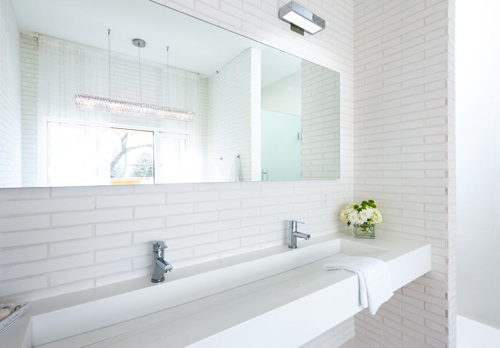 Modern inredning av ett en-suite badrum, med ett avlångt handfat, vit kakel och vita väggar