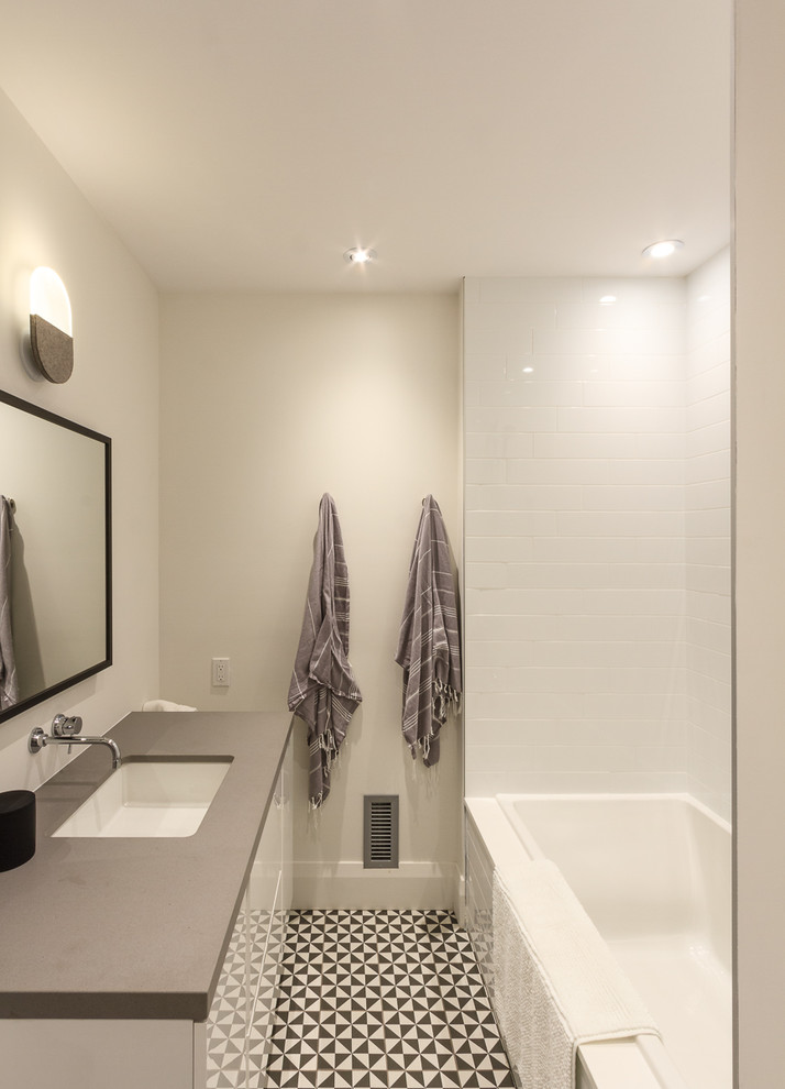 Cette image montre une petite douche en alcôve design avec un placard à porte plane, des portes de placard blanches, une baignoire en alcôve, un carrelage blanc, un carrelage métro, un lavabo encastré et un plan de toilette en quartz modifié.