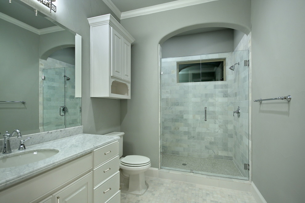 Example of a mid-sized classic white tile and stone tile marble floor alcove shower design in Dallas with an undermount sink, raised-panel cabinets, white cabinets, marble countertops, a two-piece toilet and gray walls