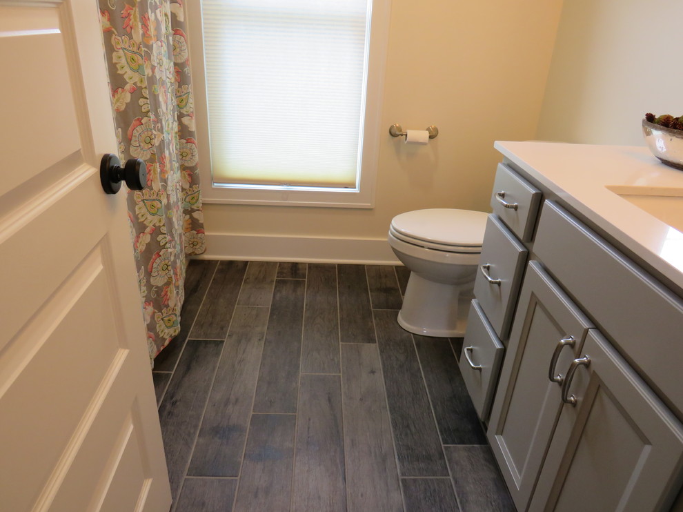 Lantlig inredning av ett mellanstort badrum med dusch, med luckor med infälld panel, grå skåp, ett hörnbadkar, en dusch/badkar-kombination, en toalettstol med separat cisternkåpa, vita väggar, linoleumgolv, ett undermonterad handfat och marmorbänkskiva