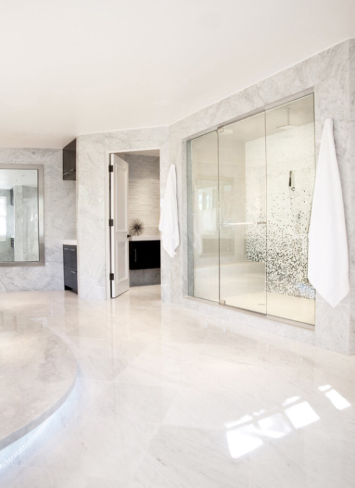Cette photo montre une très grande douche en alcôve principale tendance avec des dalles de pierre, un sol en marbre, un placard à porte plane, des portes de placard noires, une baignoire indépendante, un mur gris, un lavabo encastré et un plan de toilette en surface solide.