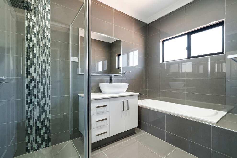 Imagen de cuarto de baño principal actual con armarios con paneles lisos, puertas de armario blancas, bañera encastrada, baldosas y/o azulejos grises, lavabo sobreencimera, suelo gris y encimeras blancas