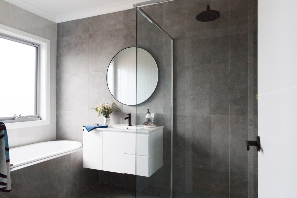 Modern inredning av ett mellanstort badrum med dusch, med vita skåp, ett platsbyggt badkar, grå kakel, grå väggar, en toalettstol med hel cisternkåpa, porslinskakel, klinkergolv i porslin, grått golv, ett integrerad handfat och släta luckor
