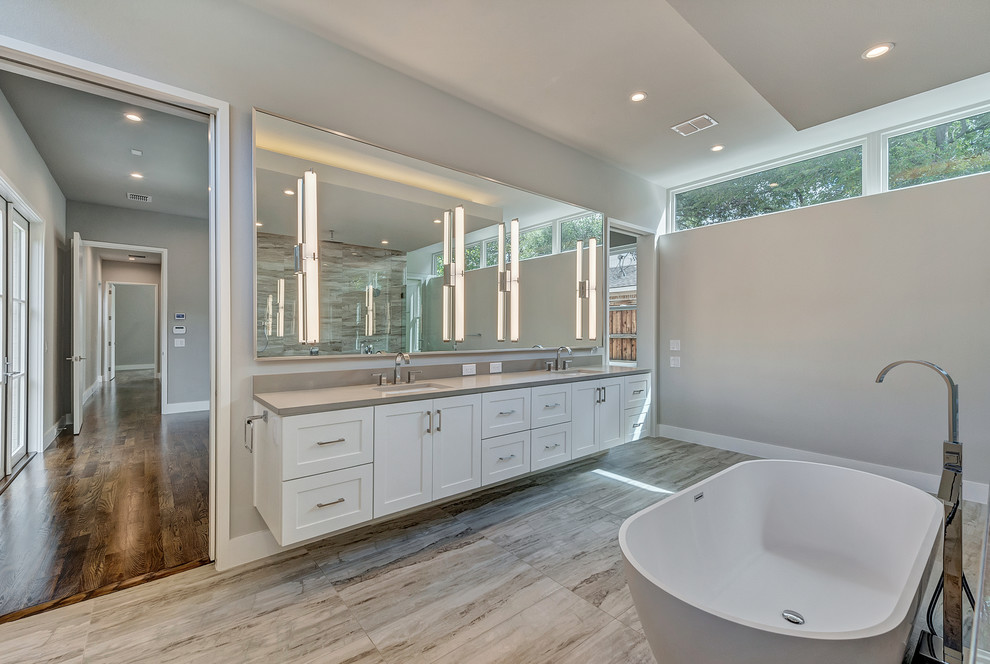 Klassisk inredning av ett en-suite badrum, med skåp i shakerstil, vita skåp, ett fristående badkar, en kantlös dusch, grå kakel, porslinskakel, grå väggar, klinkergolv i porslin, ett undermonterad handfat och bänkskiva i kvarts