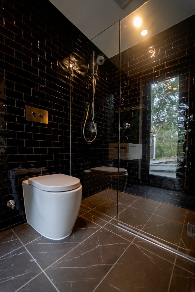 Bild på ett stort orientaliskt badrum för barn, med vita skåp, en dusch i en alkov, en toalettstol med hel cisternkåpa, svart kakel, keramikplattor, svarta väggar, marmorgolv, bänkskiva i akrylsten, svart golv och dusch med skjutdörr