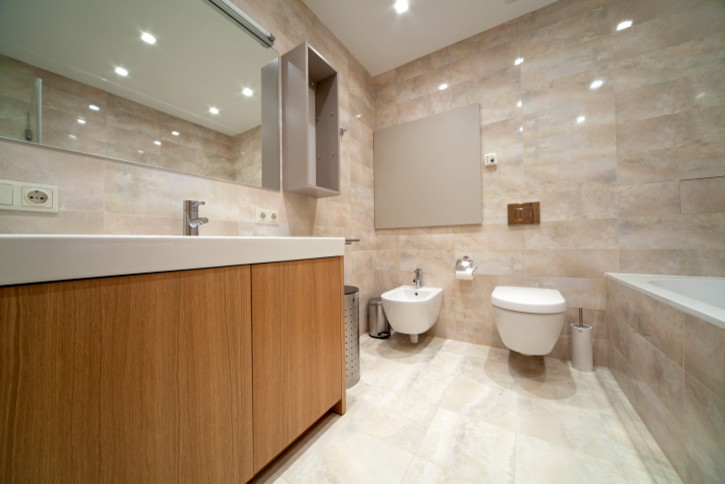 Inspiration for a large contemporary ensuite bathroom in Chicago with flat-panel cabinets, light wood cabinets, a built-in bath, a wall mounted toilet, beige tiles, ceramic tiles, beige walls, a submerged sink, solid surface worktops, a corner shower, ceramic flooring, beige floors and a hinged door.