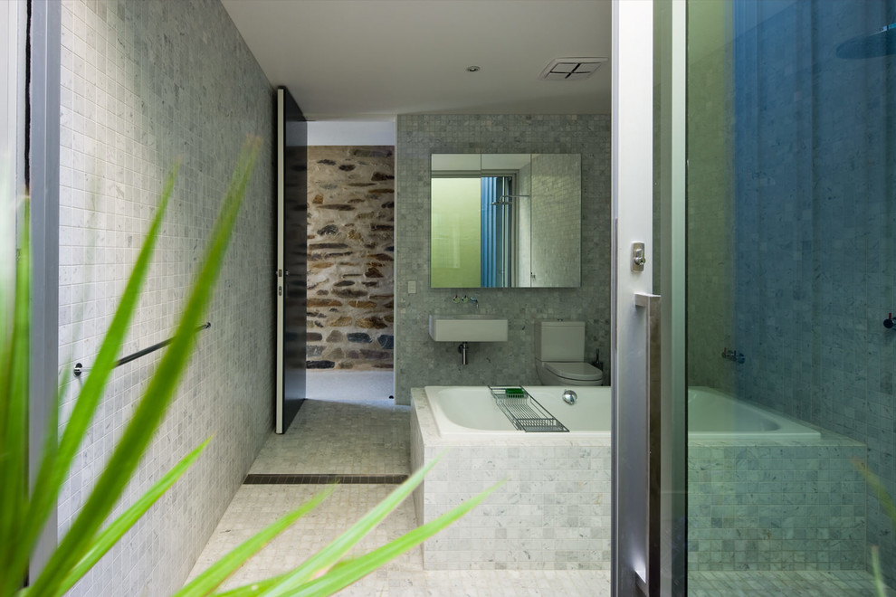 Inspiration for a medium sized contemporary ensuite bathroom in Adelaide with a wall-mounted sink, flat-panel cabinets, white cabinets, a built-in bath, a walk-in shower, a one-piece toilet, white tiles, mosaic tiles and mosaic tile flooring.