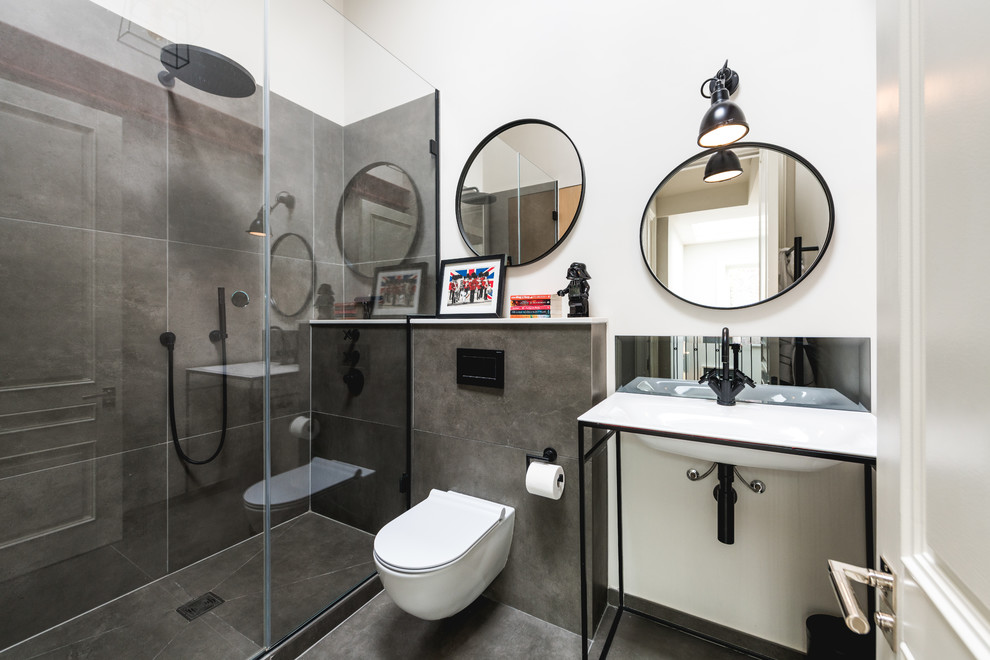 Modelo de cuarto de baño industrial de tamaño medio con sanitario de pared, baldosas y/o azulejos grises, paredes blancas, lavabo tipo consola, suelo negro y ducha con puerta corredera