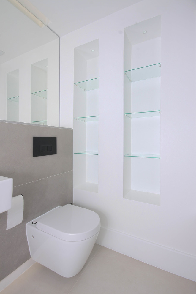 This is an example of a small contemporary ensuite bathroom in London with an alcove bath, a shower/bath combination, a wall mounted toilet, grey tiles, porcelain tiles, white walls, porcelain flooring, a wall-mounted sink and beige floors.