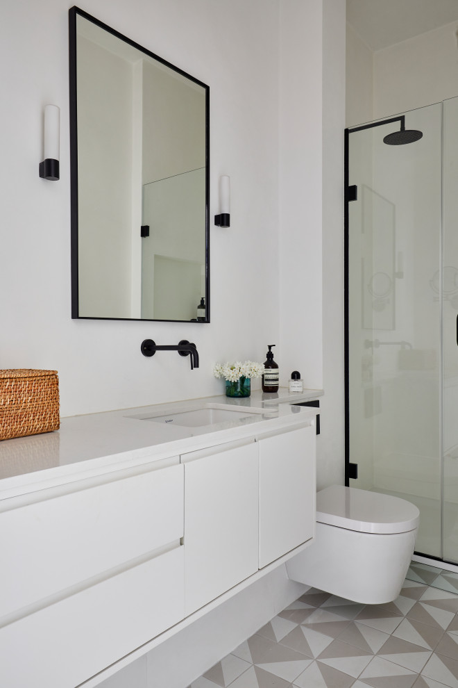 This is an example of a small contemporary ensuite bathroom in London with flat-panel cabinets, white cabinets, a walk-in shower, a wall mounted toilet, ceramic flooring, engineered stone worktops, multi-coloured floors, a single sink and a floating vanity unit.