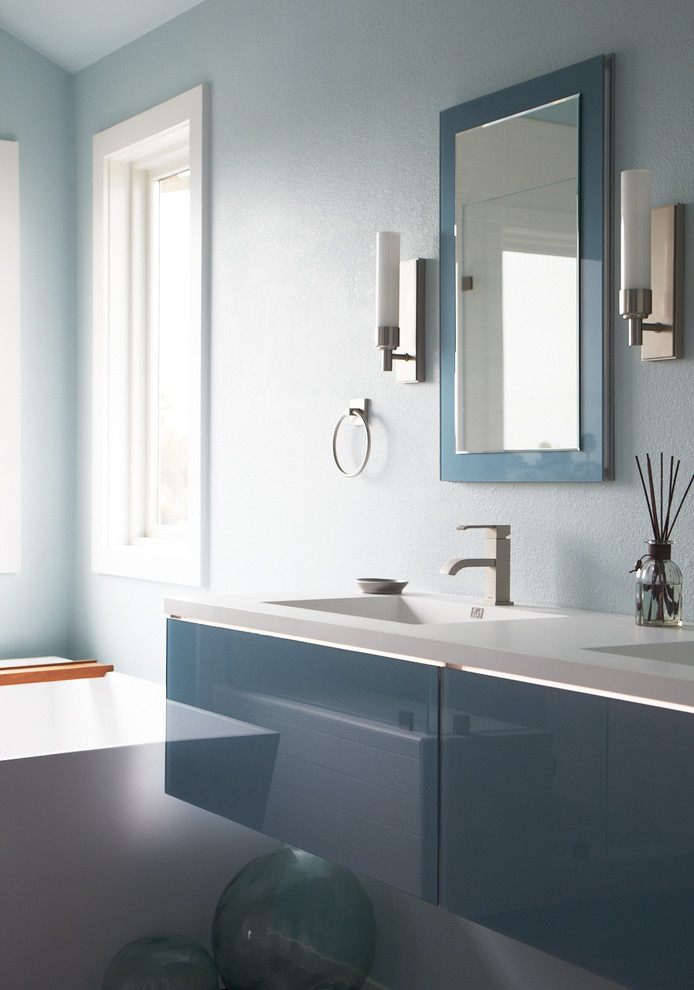 Inredning av ett modernt stort en-suite badrum, med ett väggmonterat handfat, släta luckor, blå skåp, bänkskiva i akrylsten, blå väggar, ett fristående badkar, en hörndusch, grå kakel, keramikplattor och klinkergolv i keramik