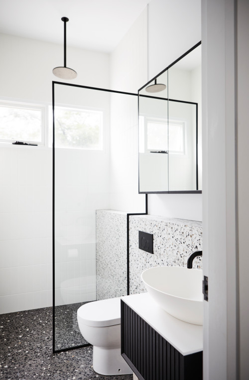 Shower ledge along the back wall of the bathroom. Black and white terrazzo tiling on the floor and wall. Matte black tapware.