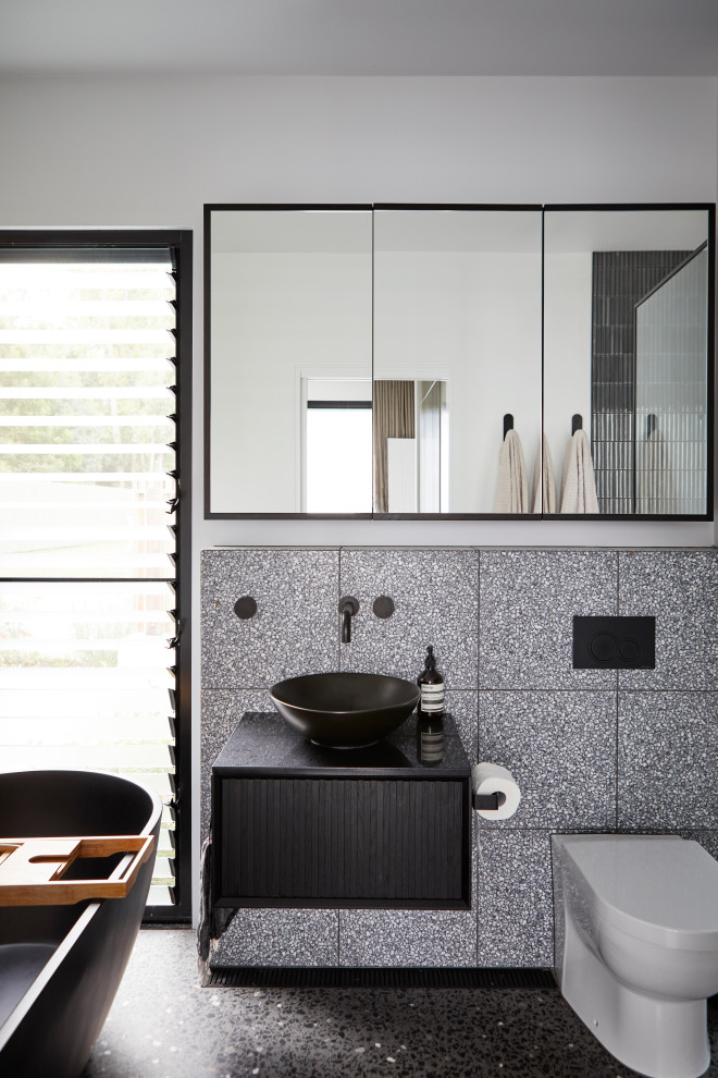 Пример оригинального дизайна: маленькая главная ванная комната в современном стиле с фасадами островного типа, черными фасадами, отдельно стоящей ванной, открытым душем, унитазом-моноблоком, черно-белой плиткой, керамической плиткой, белыми стенами, бетонным полом, настольной раковиной, столешницей из искусственного камня, черным полом, открытым душем, белой столешницей, нишей, тумбой под одну раковину и подвесной тумбой для на участке и в саду