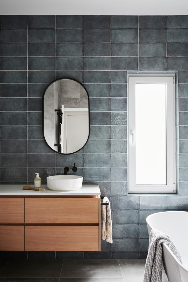 Пример оригинального дизайна: главная ванная комната среднего размера в современном стиле с плоскими фасадами, светлыми деревянными фасадами, отдельно стоящей ванной, угловым душем, синей плиткой, керамической плиткой, полом из керамогранита, настольной раковиной, столешницей из искусственного кварца, серым полом, душем с распашными дверями, белой столешницей, тумбой под одну раковину и подвесной тумбой